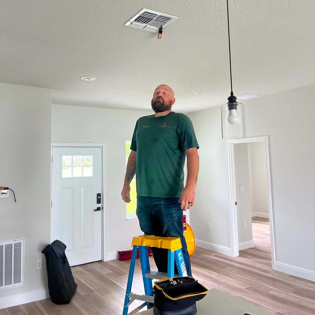 FL HVAC tech checking room-by-room airflow with calibrated instruments — part of the home walkthrough during an AC performance tune-up