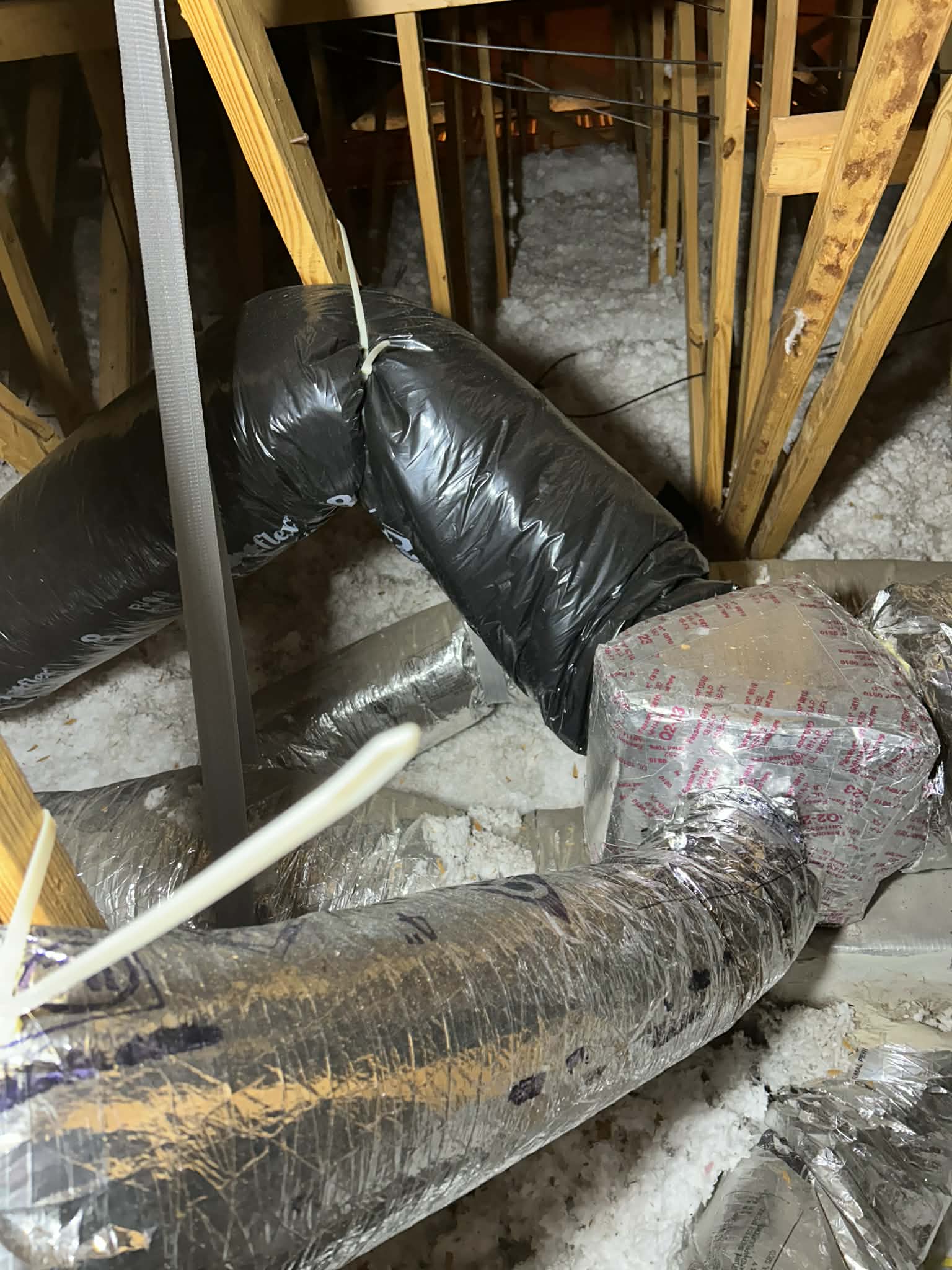 Kinked flex duct strapped tight in a Florida attic, choking the airflow to the room it serves