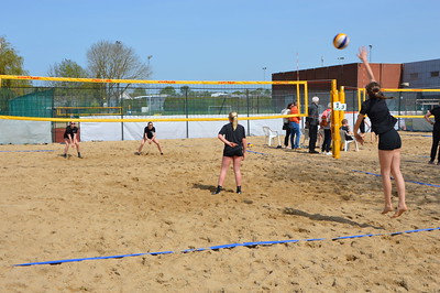 Vrouwen spelen beachvolleybal op een zonnig zandveld met een gele net en een blauwe lijn op de grond.