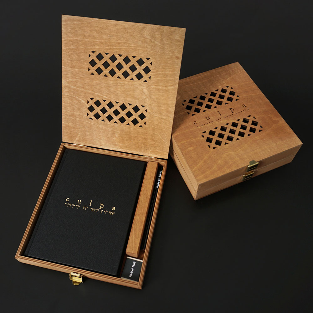 Aufgeklappte Holzbox mit schwarzen Buch Aufschrift "Culpa" Drin liegend.