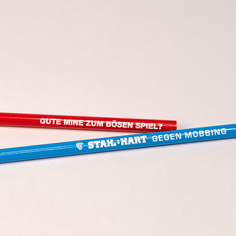 Zwei farbige Bleistifte mit Statements „Gute Mine zum bösen Spiel?“ und „Stahl:HART gegen Mobbing“ – klare Botschaften gegen Ausgrenzung.