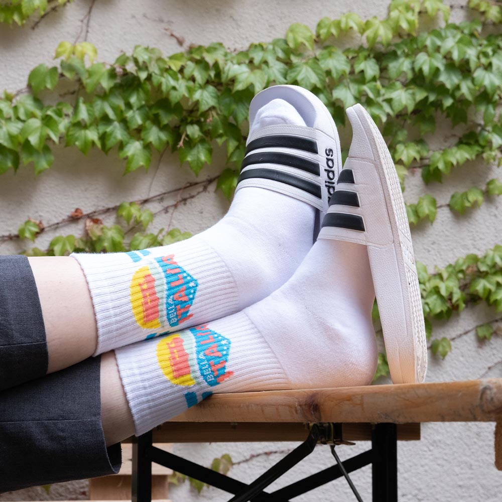 Weiße Socken mit „Bella Italia“-Motiv, getragen zu Adiletten – sommerliches RTL II-Merch.