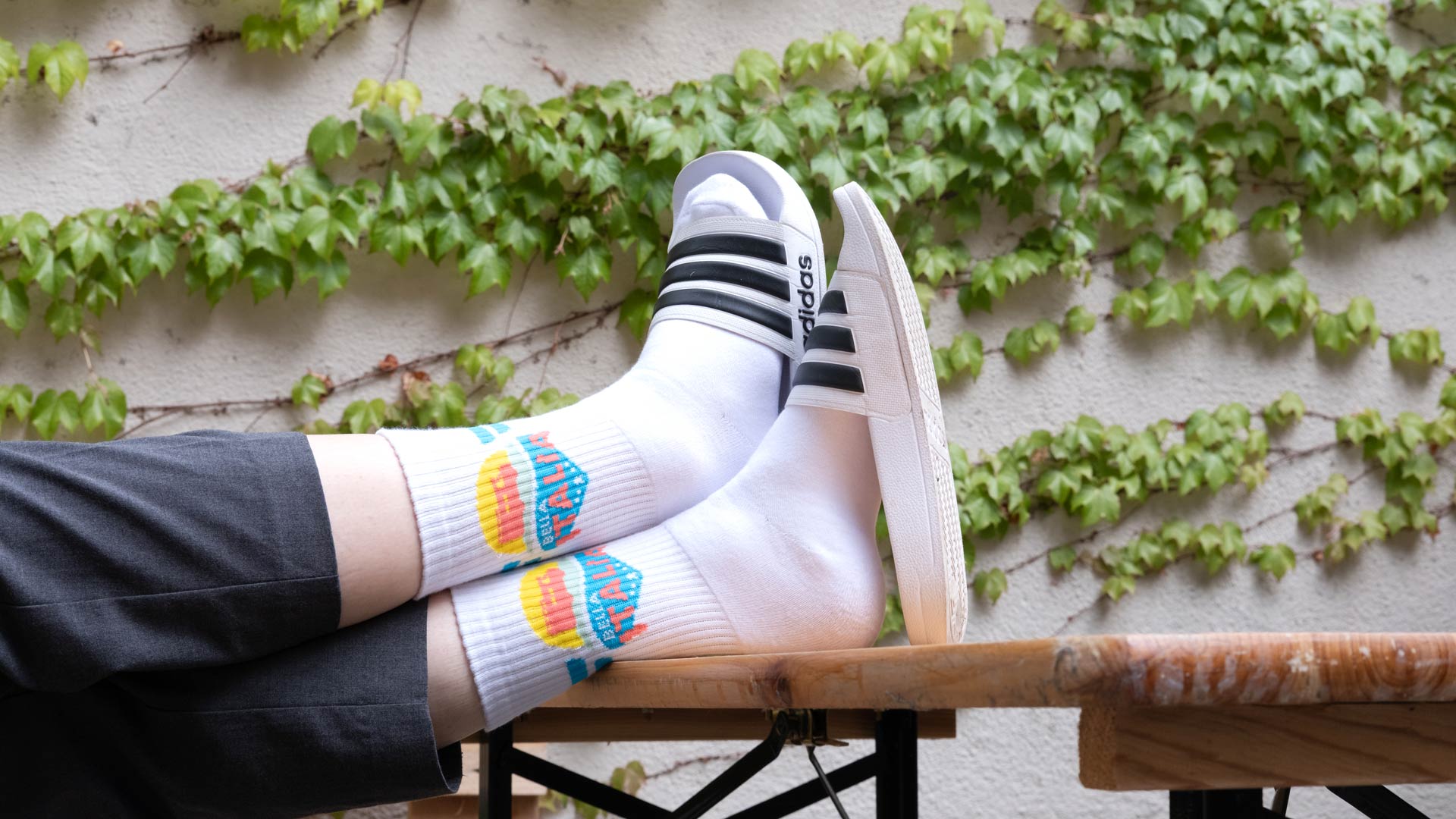 Weiße Socken mit „Bella Italia“-Motiv, getragen zu Adiletten – sommerliches RTL II-Merch.