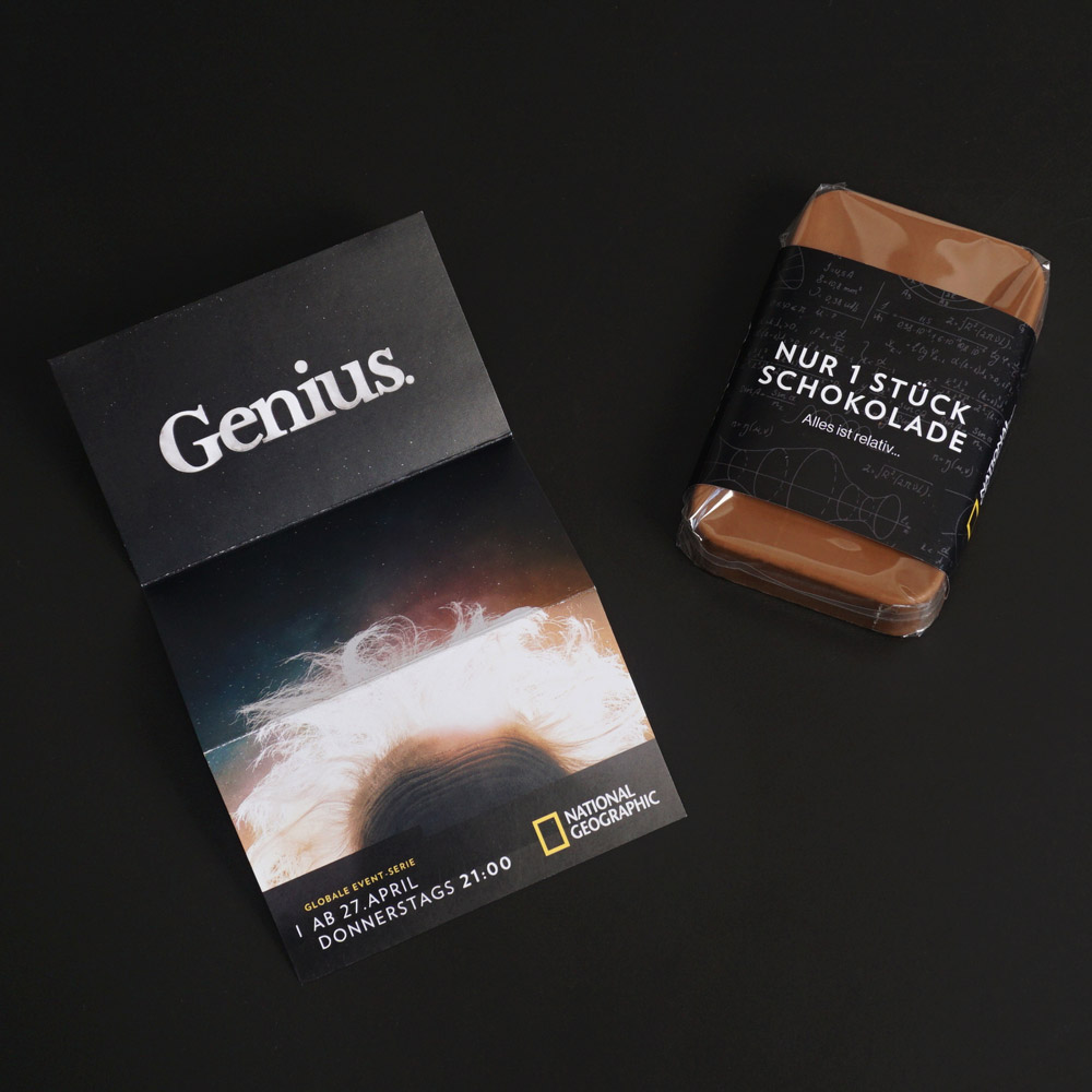 Schokoladenbar "Nur 1 Stück, alles ist relativ". Broschüre liegt daneben mit dem Titel "Genius" und dem National Geopgraphic Logo.