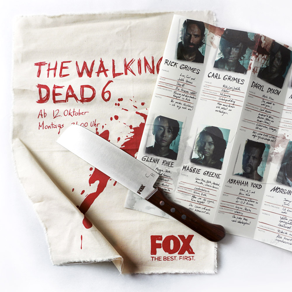 Hochwertiges Küchenmesser mit Holzgriff  auf Geschirrtuch mit FOX-Branding. Daneben liegt Flyer mit Walking Dead Schauspieler:innen.