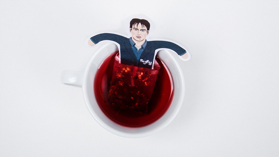 Ein personalisierter Teebeutel im Syfy-Design wird in eine Tasse mit rotem Früchtetee getaucht – Teil des humorvollen Weihnachtsmailings von NBC Universal.