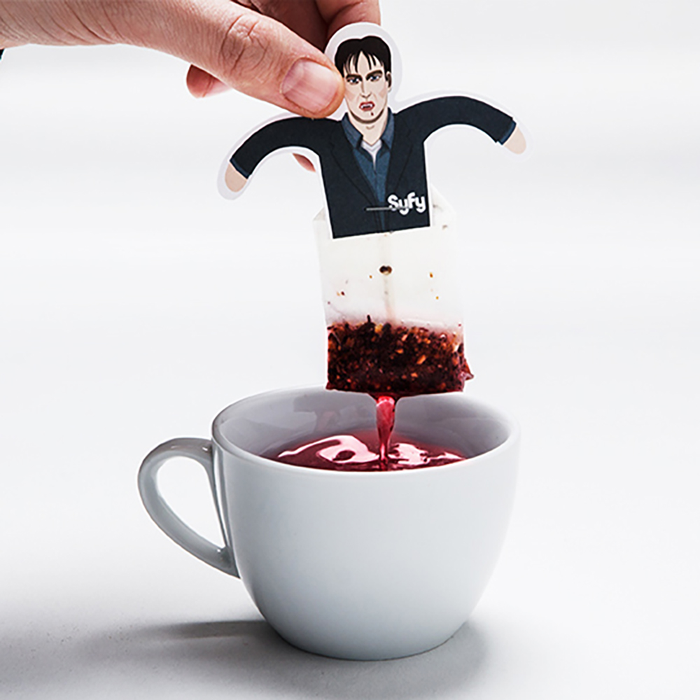 Ein personalisierter Teebeutel im Syfy-Design wird in eine Tasse mit rotem Früchtetee getaucht – Teil des humorvollen Weihnachtsmailings von NBC Universal.