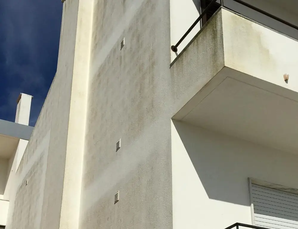 Fachada branca com manchas escuras no reboco, antes do isolamento
