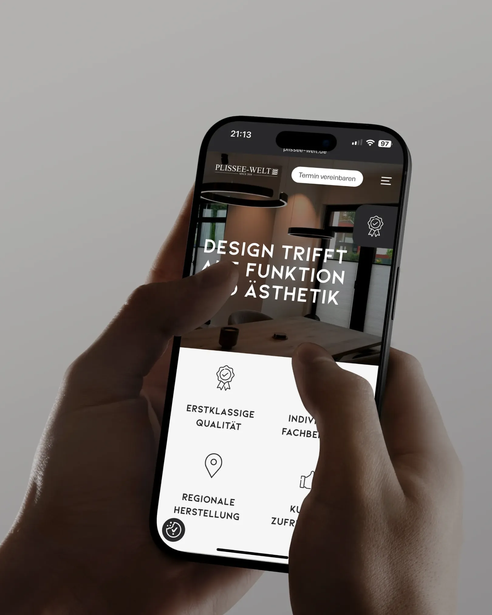 Nahaufnahme einer Hand, die ein Smartphone mit geöffneter Plissee-Welt-Website hält, auf der der Slogan „Design trifft Funktion und Ästhetik“ sowie Icons für Qualität, Fachberatung, regionale Herstellung und Kundenzufriedenheit zu sehen sind