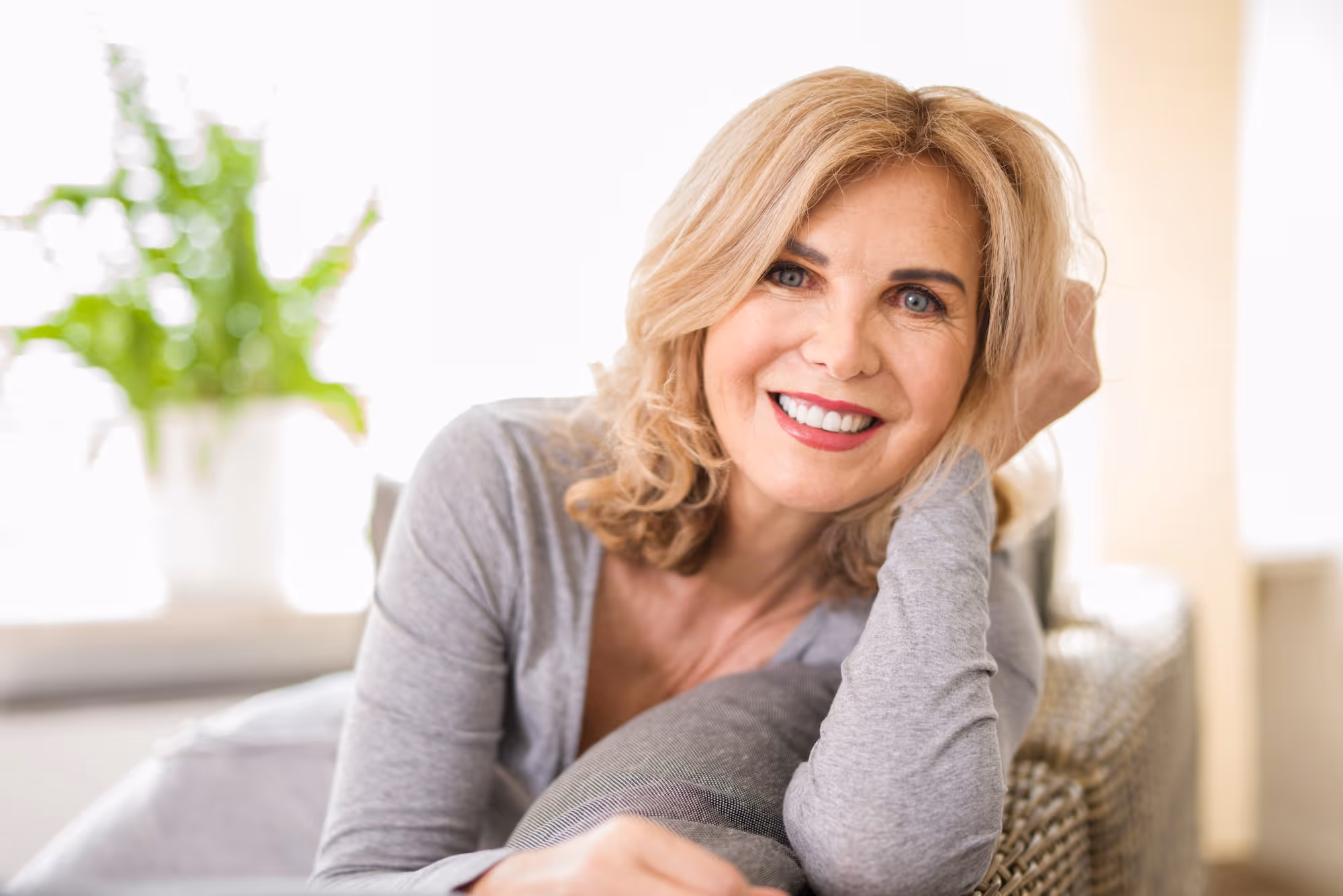 A woman sitting on top of a couch next to a potted plant.