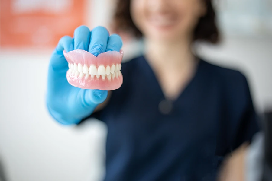 A woman in scrubs holding up a set of dentures.