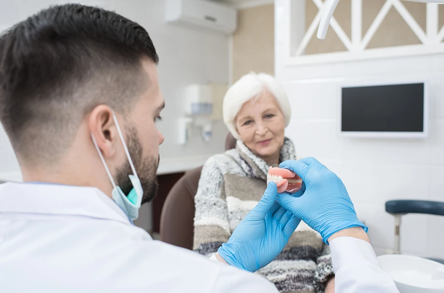 A woman sitting in a dentist surgery being shown a set of dentures by a dentist.