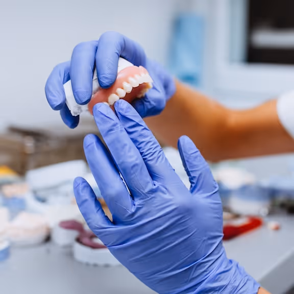 A person in blue gloves holding a set of dentures.