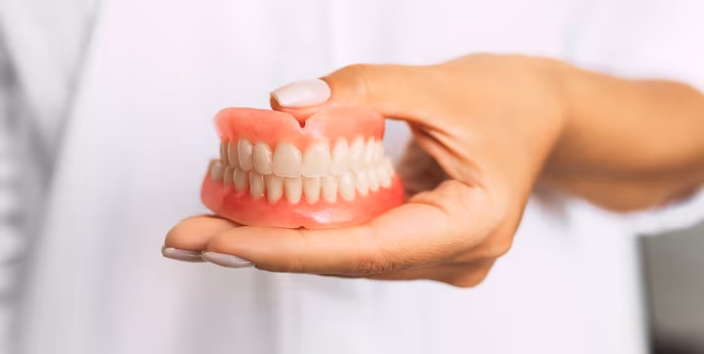 A person holding a set of dentures in their hand.