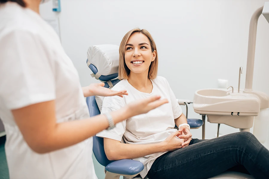 A woman sitting in a dental chair talking to a dentist.