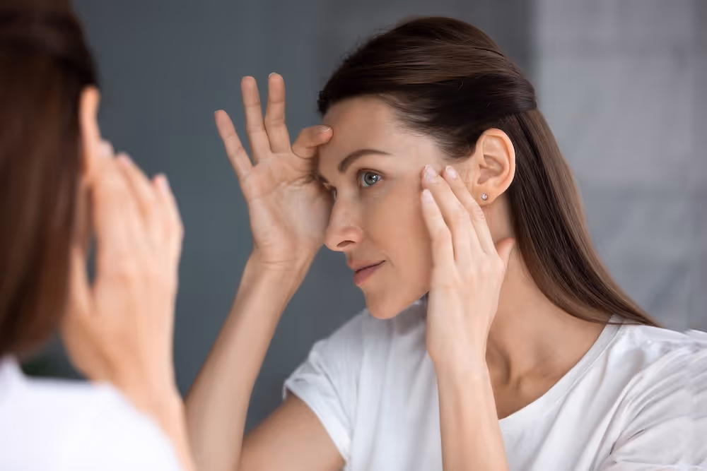 A woman looking at her face in the mirror.