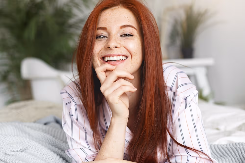 A woman with long red hair laying on a bed.