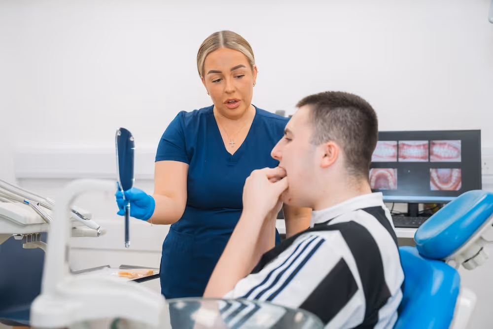 Dentist showing a handheld mirror to a male patient sitting in a dental chair.