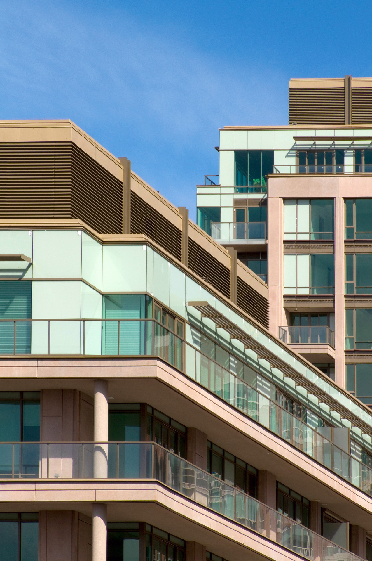 Close-up view of the condominium façade showing glass balconies, limestone cladding, and stepped terraces.