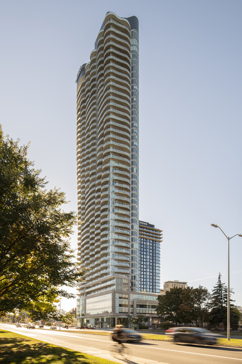 Tall modern high-rise building with curved balconies along a busy street under a clear blue sky.