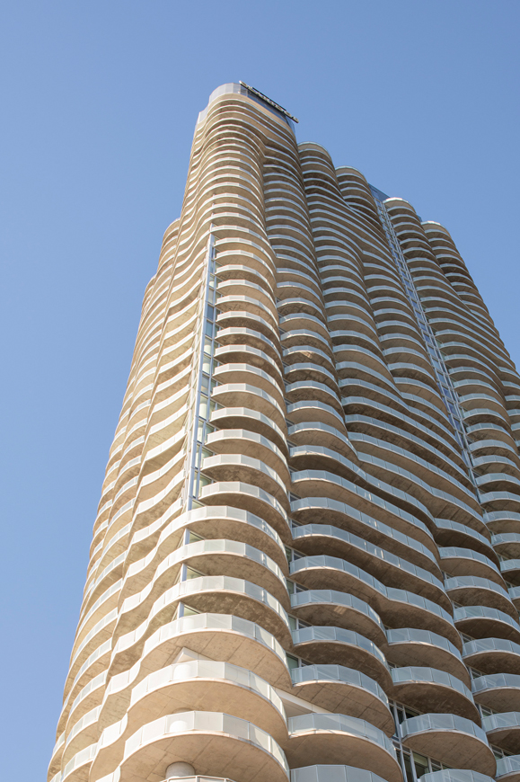 Modern high-rise residential building with curved glass balconies against a clear blue sky.