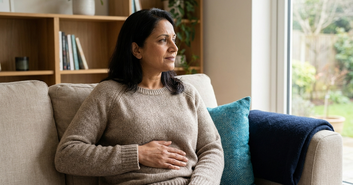 Woman in her forties resting a hand on her upper right abdomen at home, a common sign of gallbladder pain