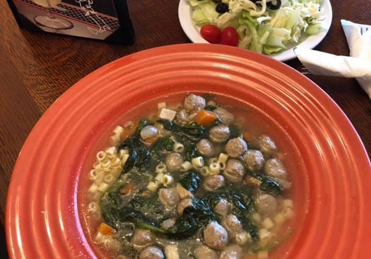A bowl of soup with meatballs and greens.