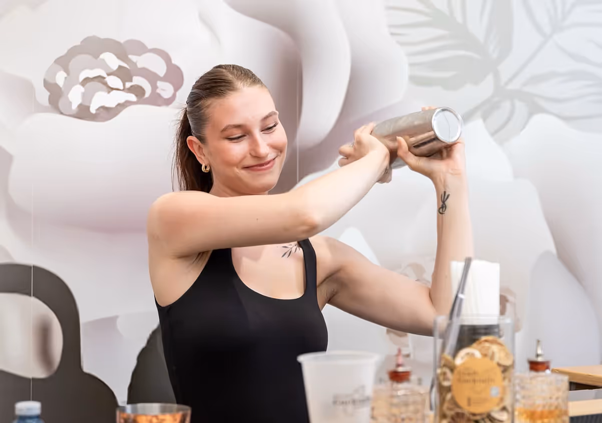 Young woman smiling while shaking a cocktail shaker behind a bar.