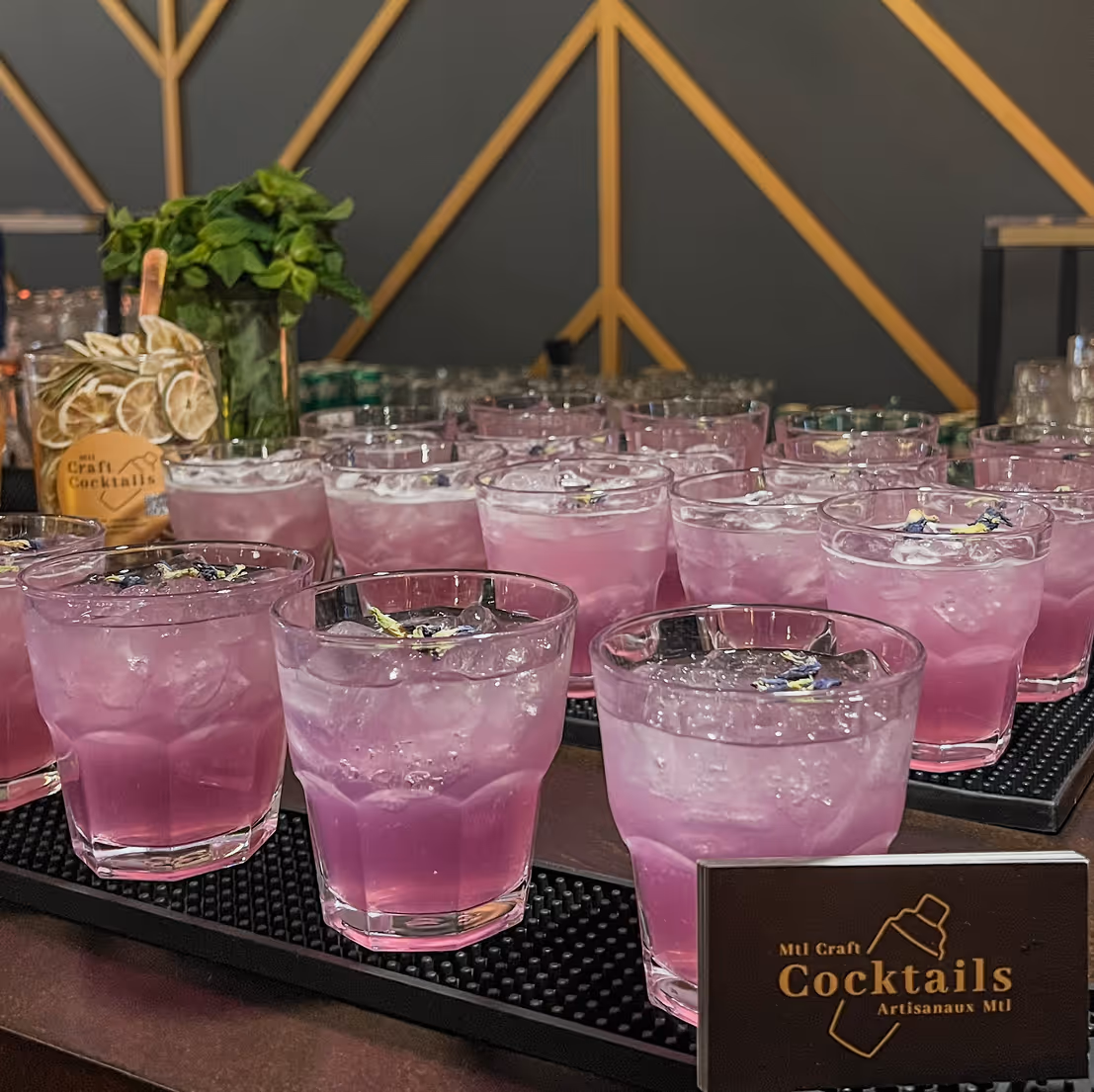 Tray of purple craft cocktails with ice and flower garnish on a mobile bar counter.