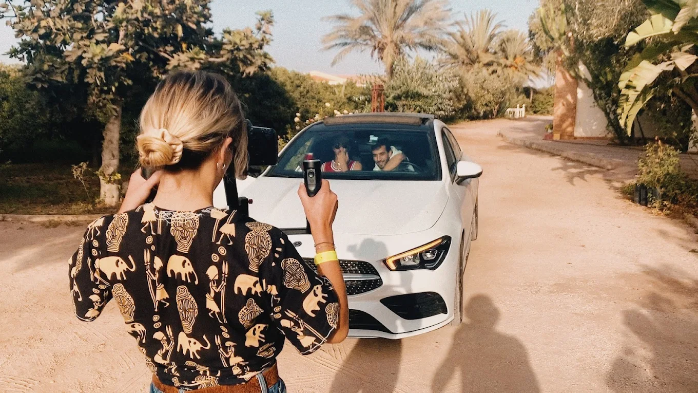 une jeune femme blonde qui filme un clip musical. Une voiture blanche au maroc