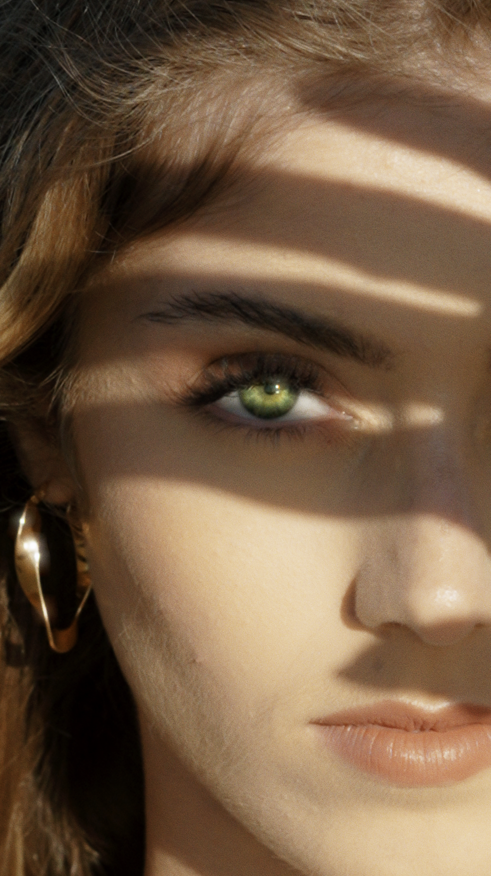 visage d'une jeune femme aux yeux vert, qui se protège du soleil en plaçant sa main devant son visage