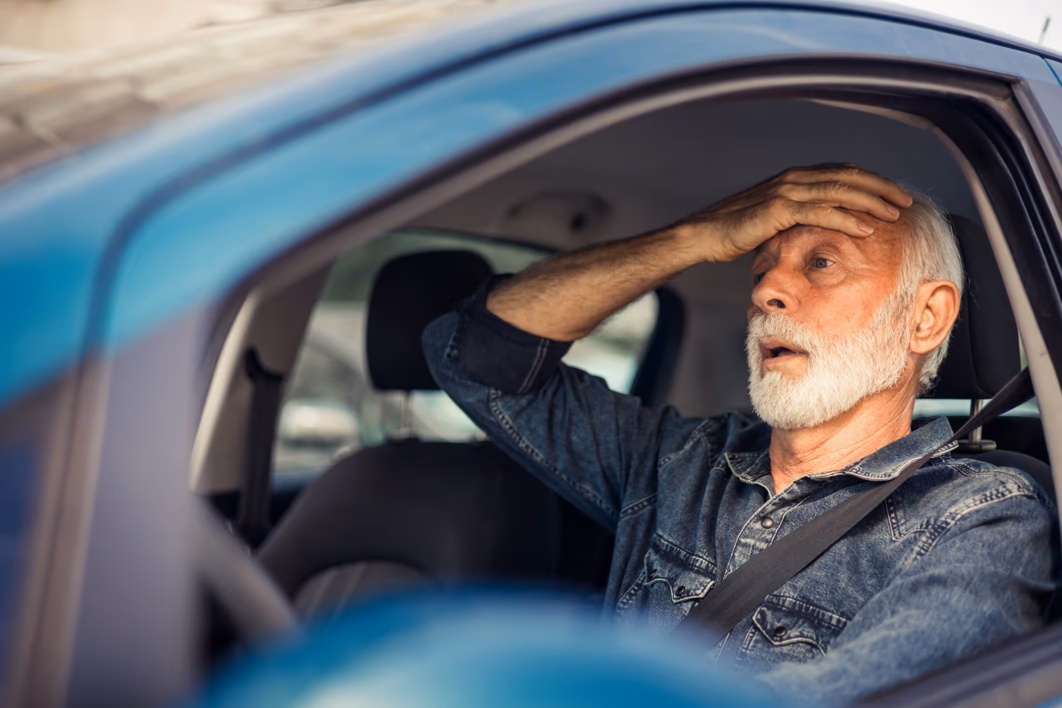 Elderly man holding his head in pain inside a vehicle, representing types of brain injuries from car accidents.