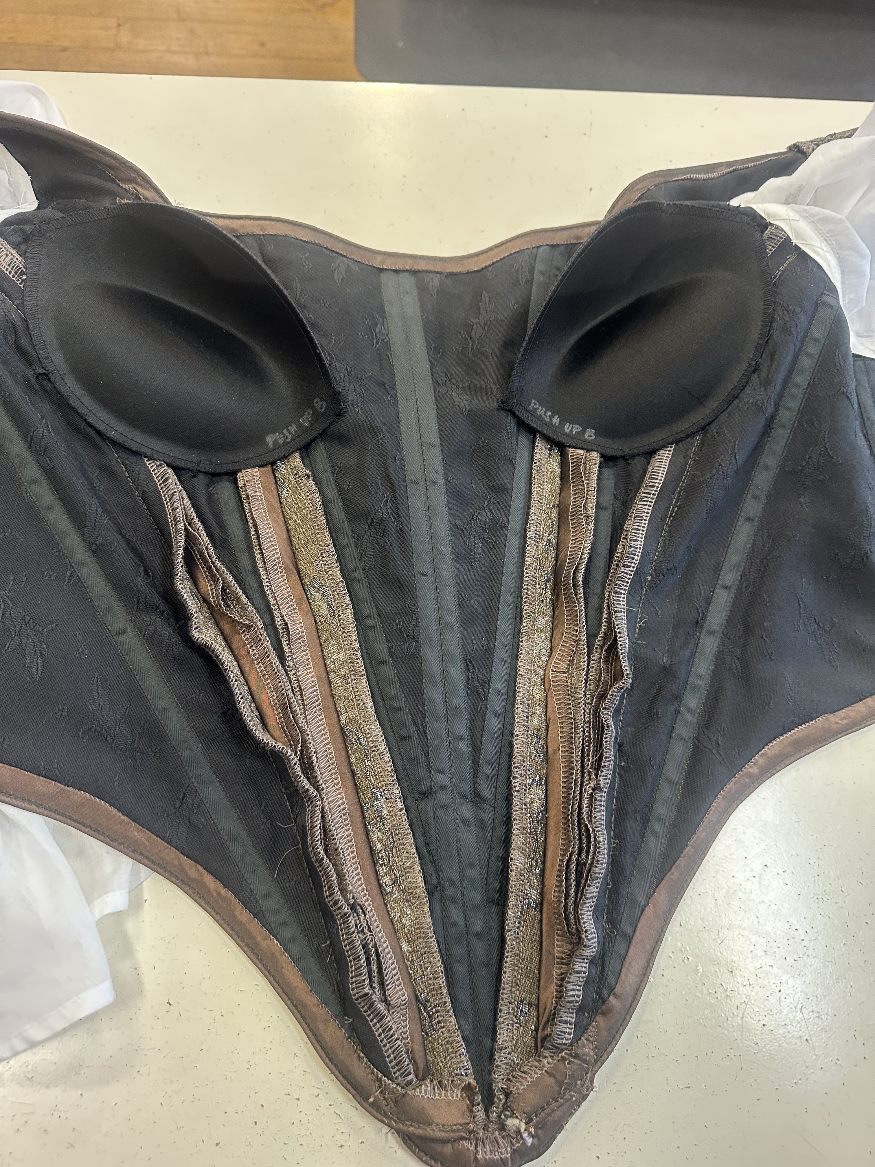 A picture of the inside of a brown bodice, showing bust pads and black corset layer