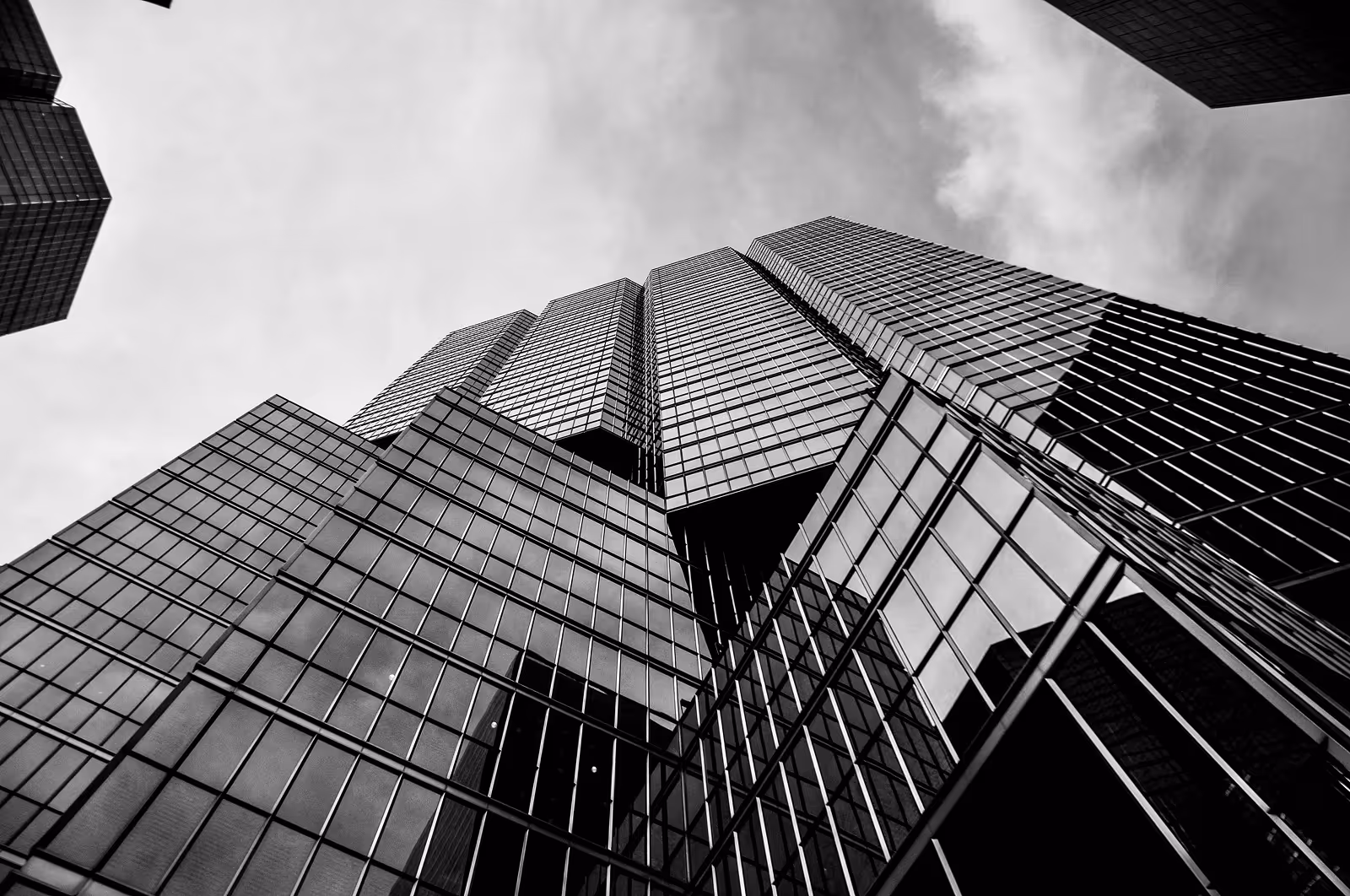 Black and white low-angle view of modern glass skyscrapers against a cloudy sky.