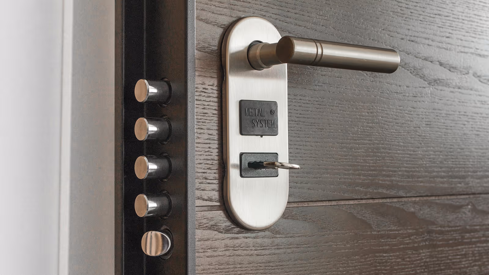 Close-up of a modern door lock with a metal handle, a key inserted, and four large metal locking bolts on the door frame.