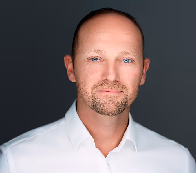 Portrait of a man with blue eyes and a trimmed beard wearing a white collared shirt.