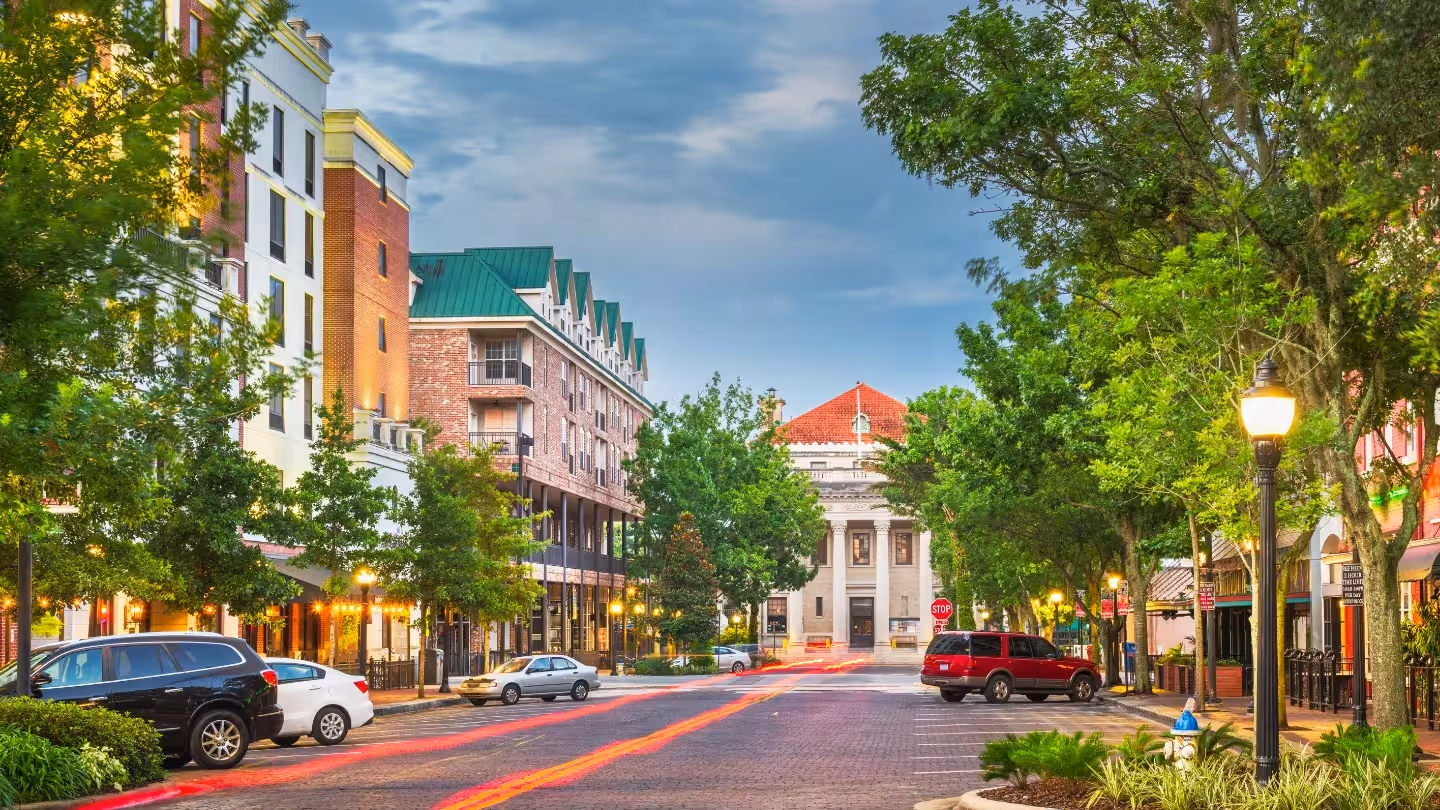 City skyline at sunset with a river and bridge in the foreground under a clear blue sky.