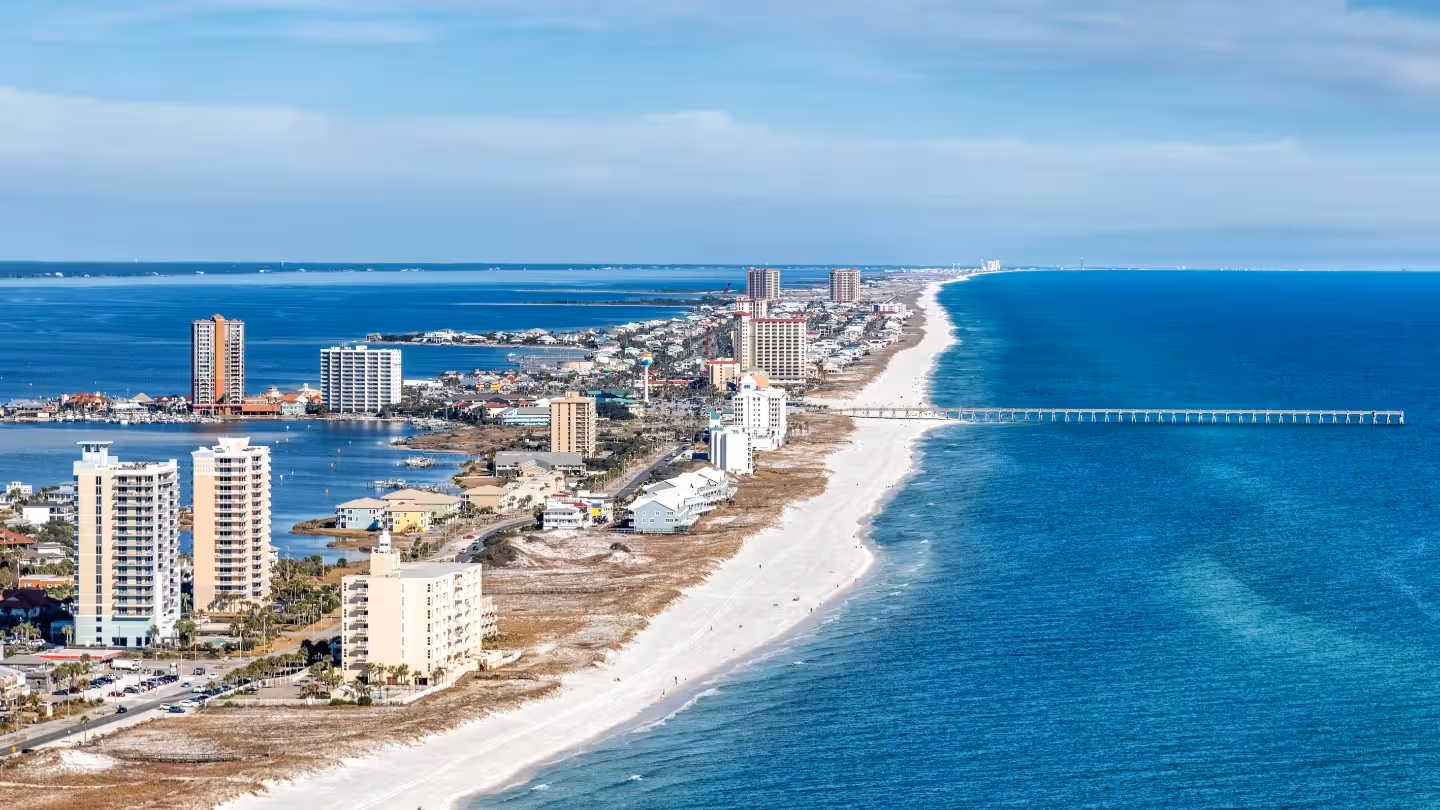City skyline at sunset with a river and bridge in the foreground under a clear blue sky.