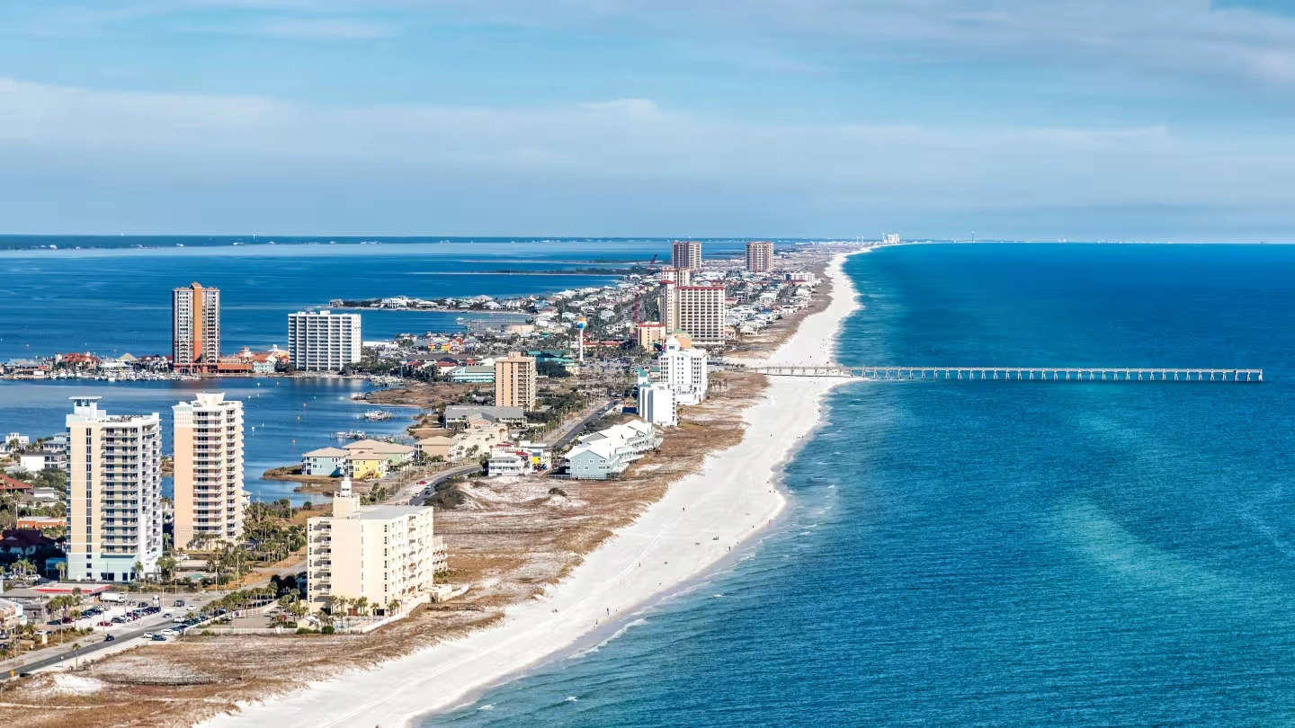 City skyline at sunset with a river and bridge in the foreground under a clear blue sky.