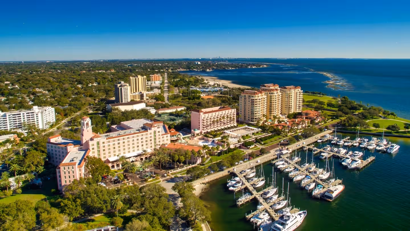 City skyline at sunset with a river and bridge in the foreground under a clear blue sky.