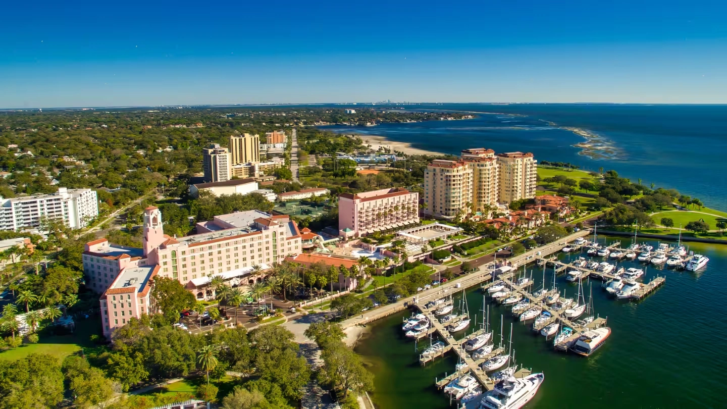 City skyline at sunset with a river and bridge in the foreground under a clear blue sky.