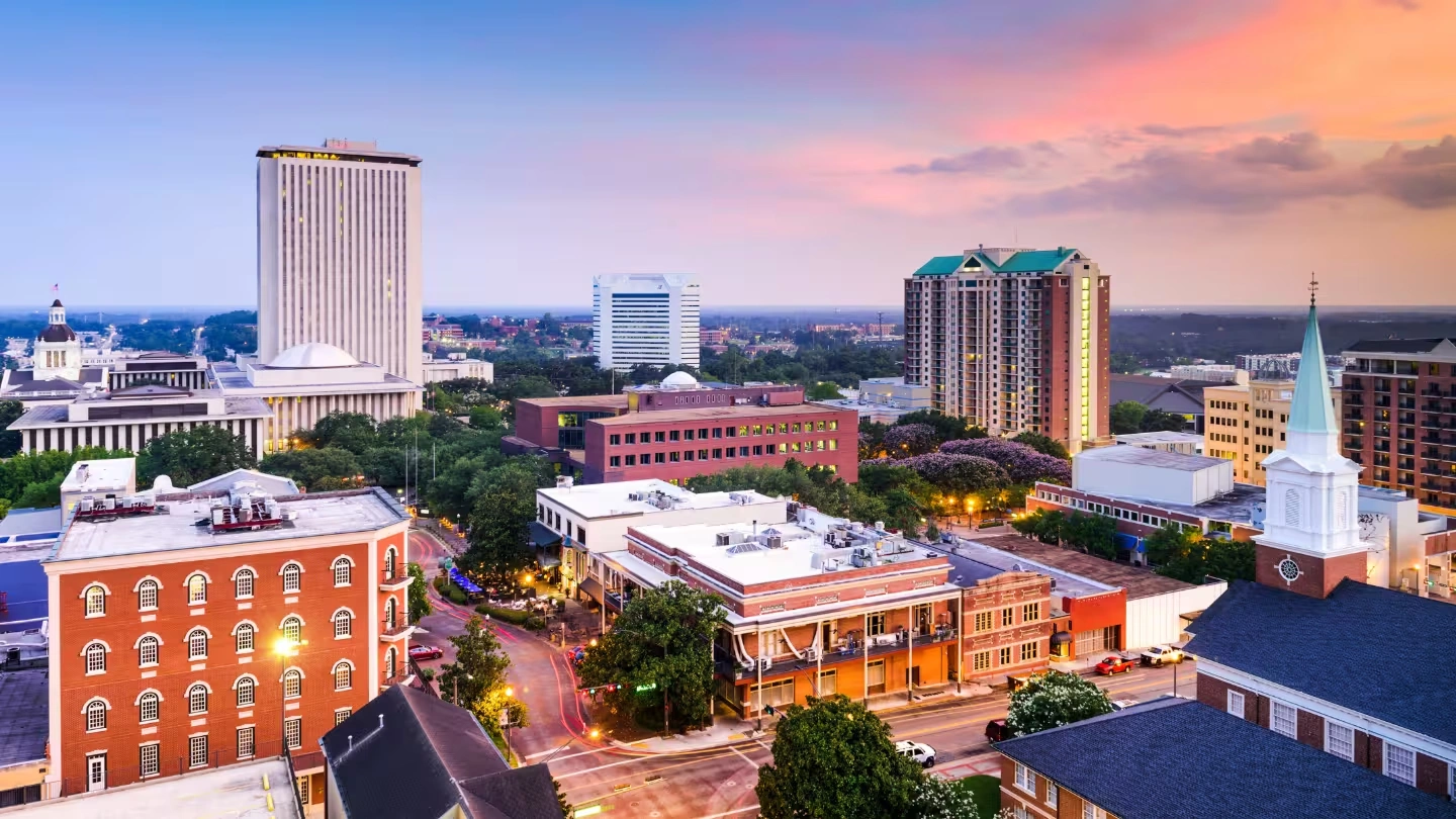 City skyline at sunset with a river and bridge in the foreground under a clear blue sky.