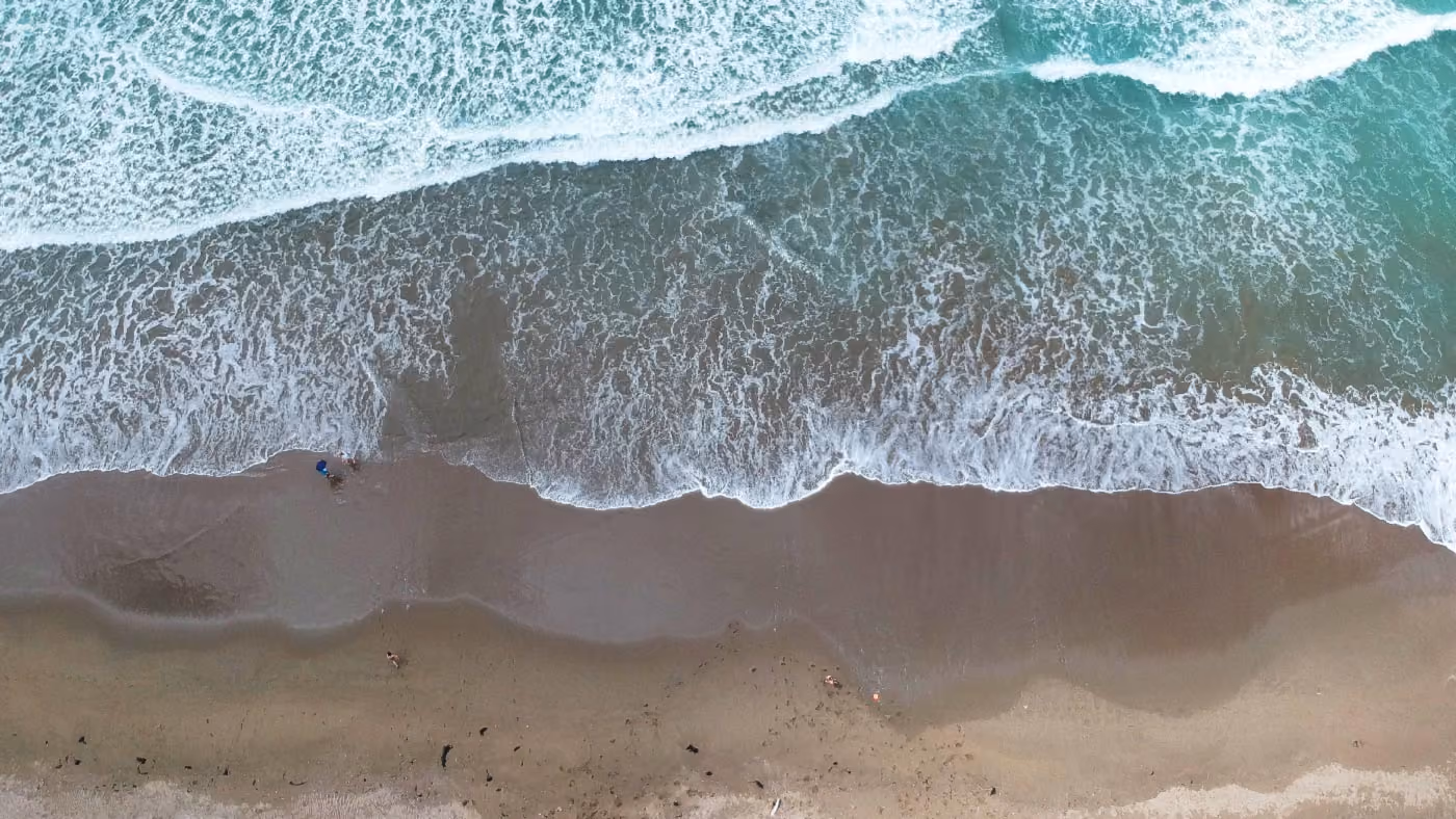 An aerial photo looking down at beach and surf, taken by a drone.