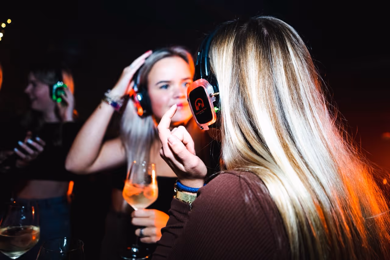 Twee jonge vrouwen op een silent disco evenement dragen kleurrijk verlichte koptelefoons terwijl ze samen dansen en genieten van een drankje.