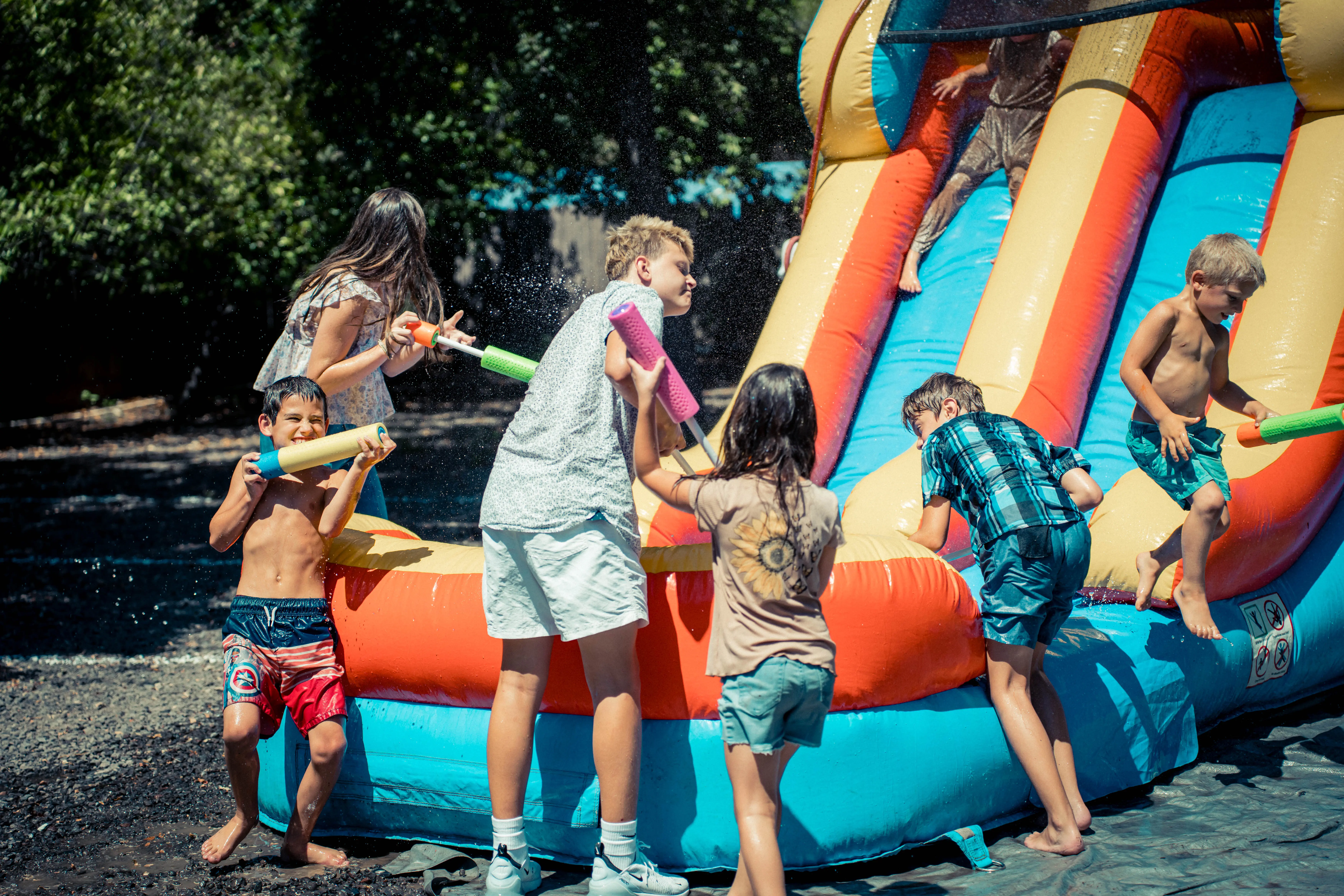Kids playing with water blasters and climbing on an inflatable water slide outside.