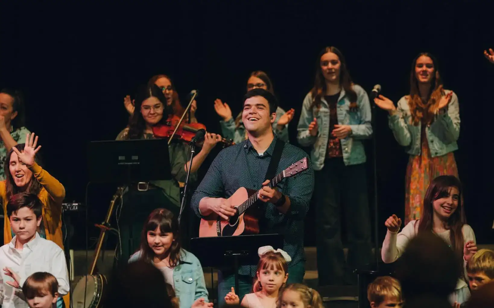 Worship team and children singing and praising together on stage at EFCC Chico, with a guitarist leading and people clapping and raising hands in celebration.
