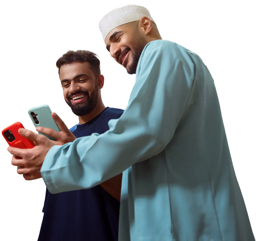 رجلان يبتسمان وينظران إلى هواتف، أحدهما بزي تقليدي أزرق فاتح وقبعة بيضاء.