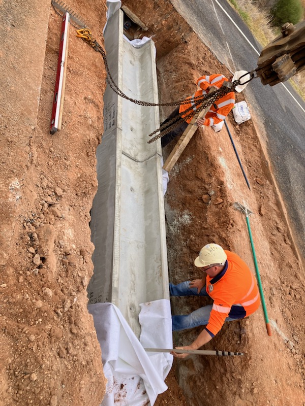 Workers placing a precast concrete culvert in a hole cut out of the road
