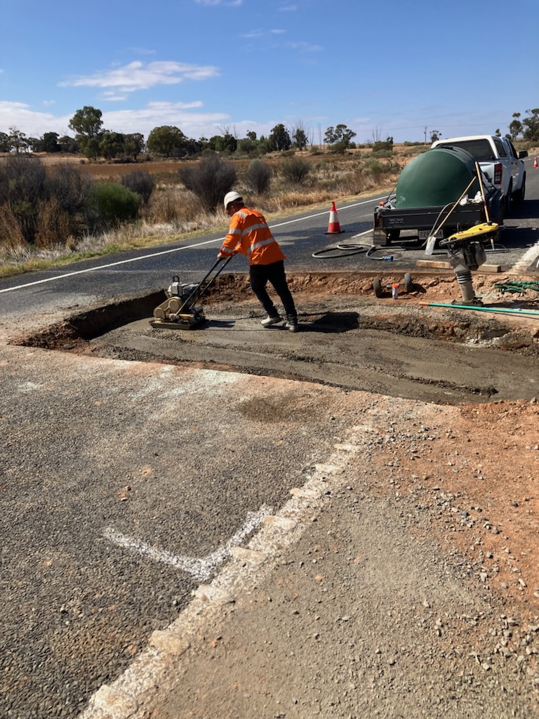 Workers working on a cut section of road for a culvert project
