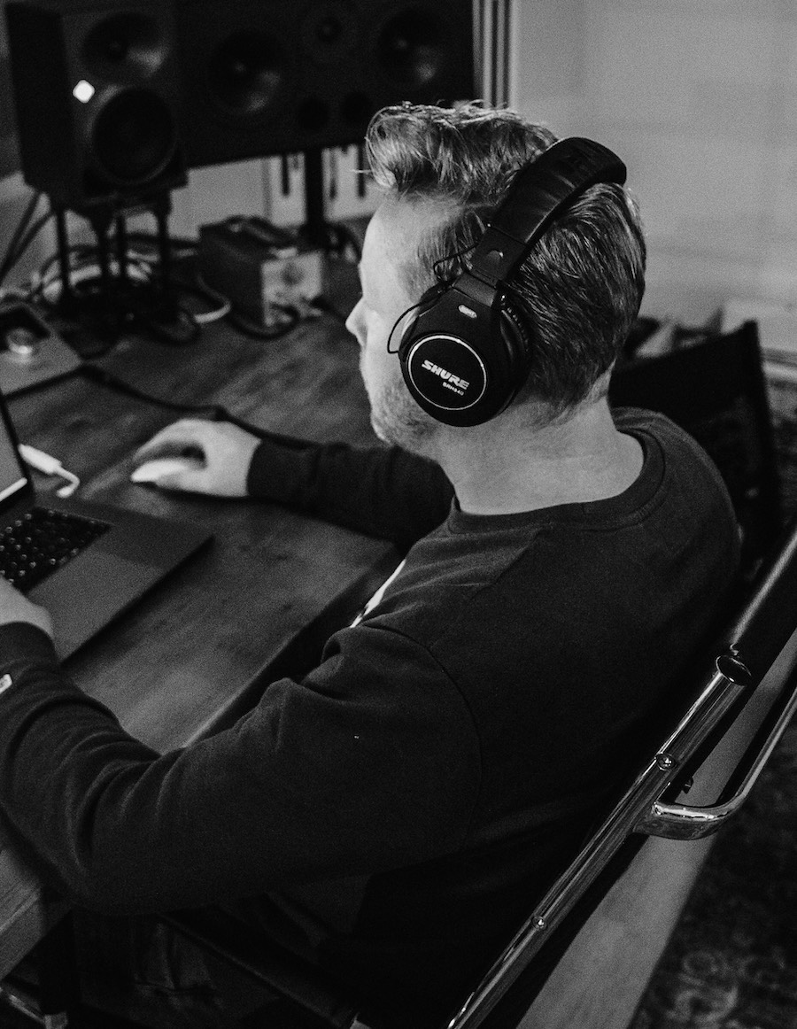 Adam Dekker met koptelefoon achter zijn bureau werkend op een laptop, met studiomonitoren op de achtergrond.